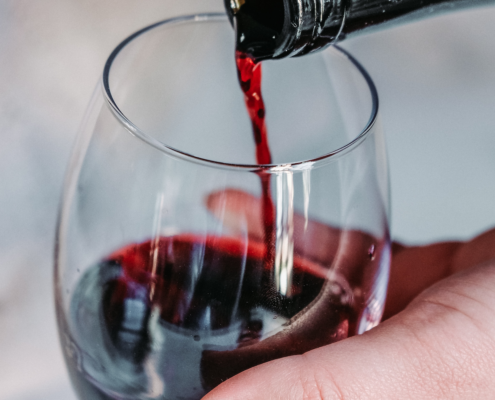 woman's hand holding a stemless wine glass while she pours Malbec wine into it from a dark bottle