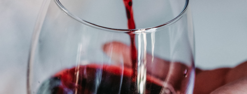 woman's hand holding a stemless wine glass while she pours Malbec wine into it from a dark bottle