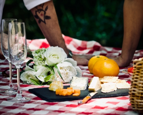 closeup of a red and white picnic blanket with some food and a man and woman's hands in the background