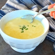 Closeup of creamy sweet corn soup with a sprinkle of chives being lifted from the bowl with a silver soup spoon