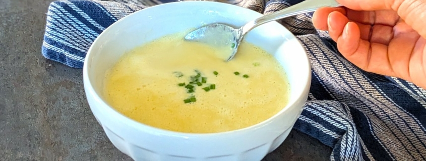 Closeup of creamy sweet corn soup with a sprinkle of chives being lifted from the bowl with a silver soup spoon