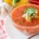 closeup of heirloom tomato gazpacho in a glass bowl on a red and white napkin with garlic, tomato and a yellow pepper in the background