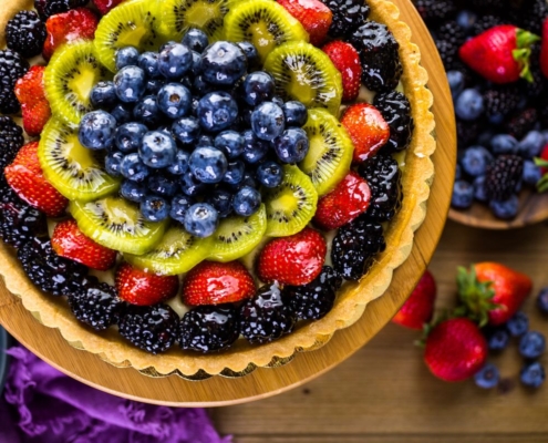 The Best French Fruit Tart Recipe 1 closeup of a French fruit tart on a brown background with berries scattered in the background