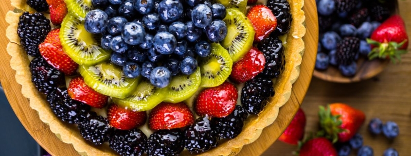 closeup of a French fruit tart on a brown background with berries scattered in the background