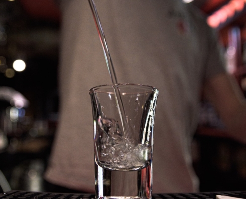 closeup of a shot glass with a bartender pouring grape vodka into it