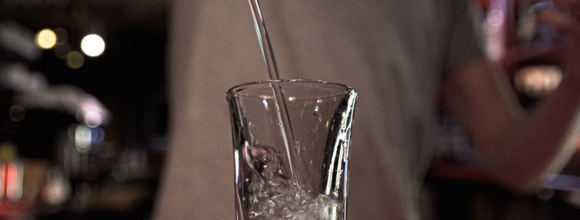 closeup of a shot glass with a bartender pouring grape vodka into it