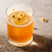 Cognac elderflower cocktail on a beige background with scattered chamomile flowers