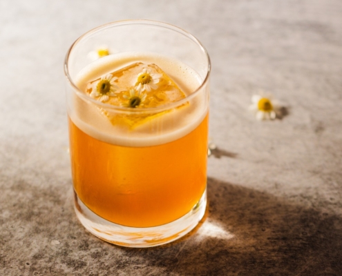 Cognac elderflower cocktail on a beige background with scattered chamomile flowers