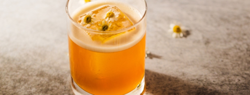 Cognac elderflower cocktail on a beige background with scattered chamomile flowers