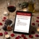Closeup of the product the Passion Pantry Audit on a tablet placed on a wooden table beside a glass of wine, a candle and rose petals