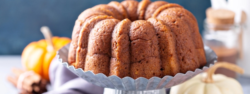 closeup of a pumpkin bundt cake on a tin cake stand with two pumpkins in the background