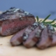 closeup of a medium steak on a cutting board with a sprig of rosemary behind it