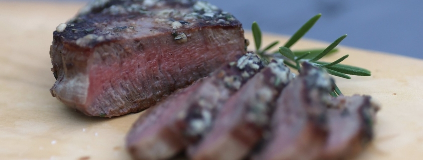 closeup of a medium steak on a cutting board with a sprig of rosemary behind it