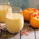 two pumpkin pie protein shakes on a wooden table with mini pumpkins and autumn leaves