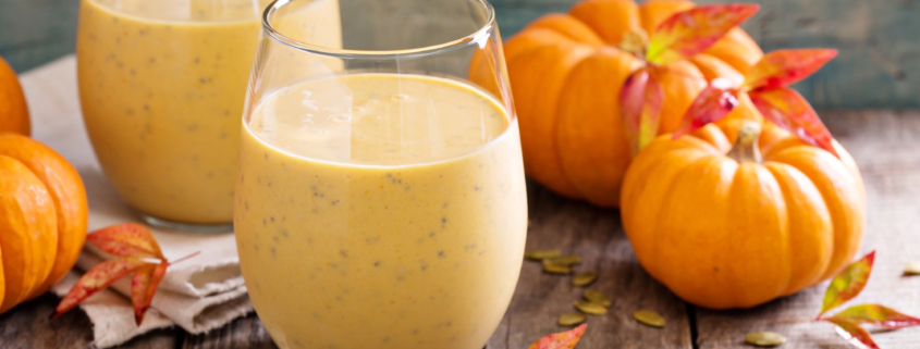 two pumpkin pie protein shakes on a wooden table with mini pumpkins and autumn leaves