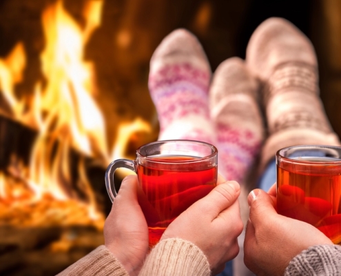 couple's hands holding sorrel hot toddy's in front of a roaring fire