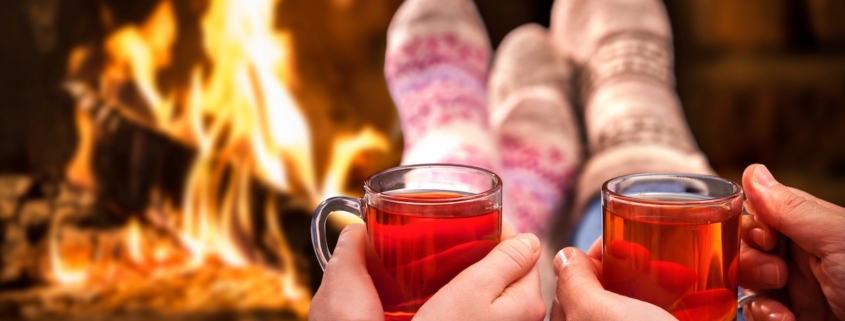 couple's hands holding sorrel hot toddy's in front of a roaring fire