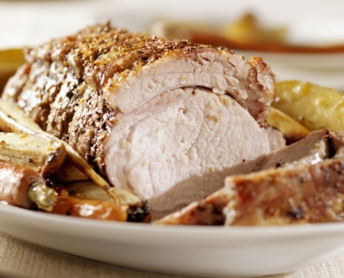 Closeup of oven roasted pork loin with vegetables on a white plate