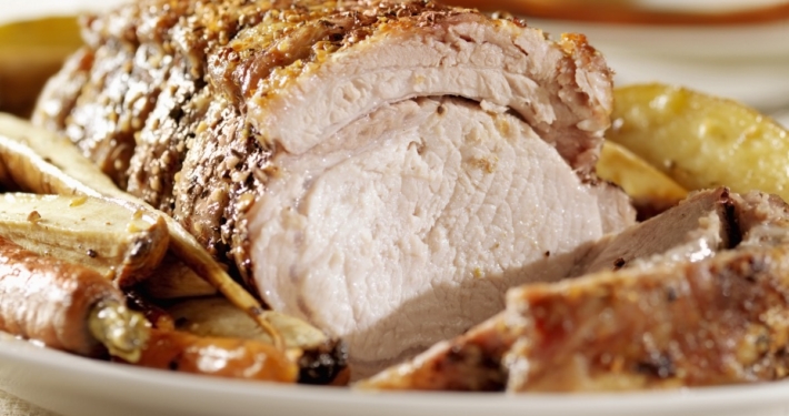 Closeup of oven roasted pork loin with vegetables on a white plate