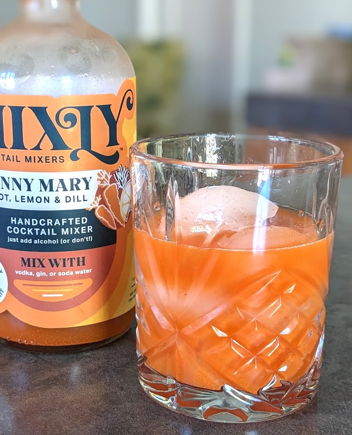 closeup of a carrot juice bloody mary with the mixly mixer bottle in the background.