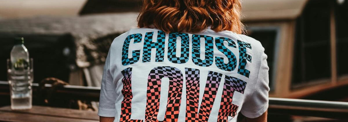 the back of a seated woman who is wearing a tee-shirt printed with the words "choose love."