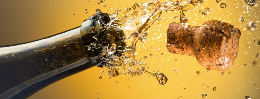 closeup of cork shooting out of a bottle of champagne