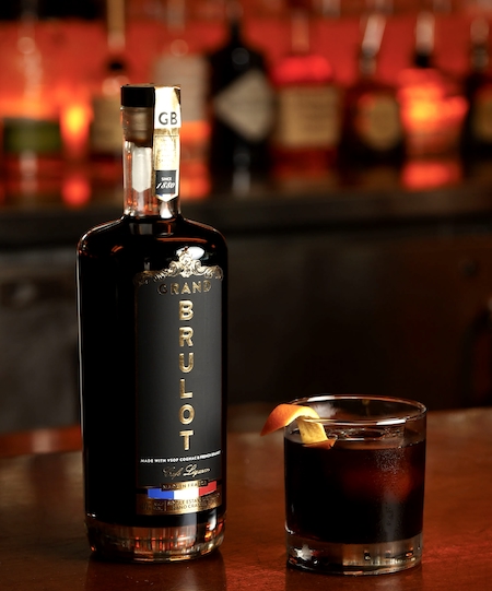 cognac espresso old fashioned sitting on a bar next to a bottle of grand brulot