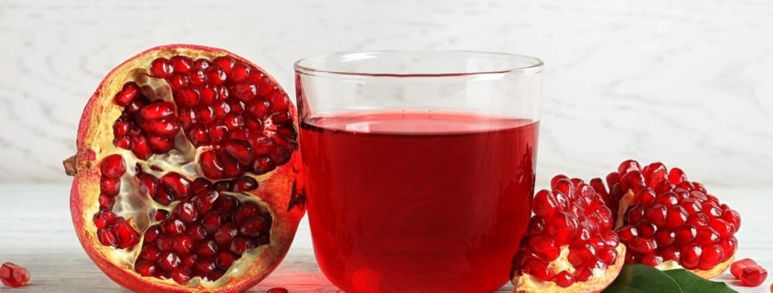 Closeup of a half pomegranate and two quarters plus a glass of pomegranate juice on a white background
