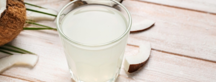Glass of coconut water with slices of coconut in the background