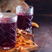 closeup of two glasses of the hot tart cherry mocktail on a wooden board with scattered raisins, almonds and citrus peel