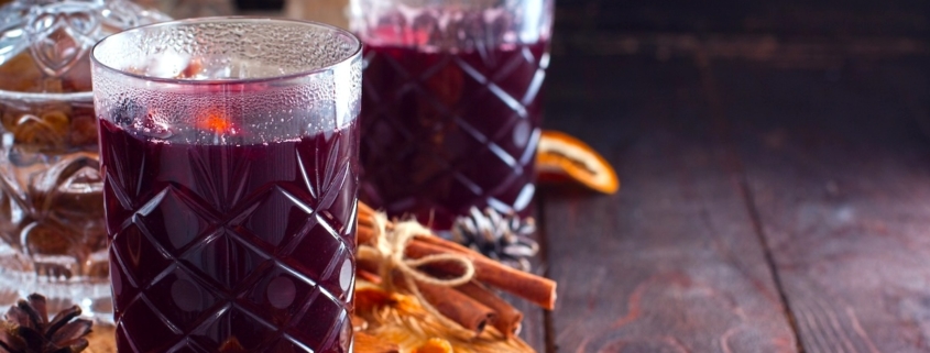 closeup of two glasses of the hot tart cherry mocktail on a wooden board with scattered raisins, almonds and citrus peel