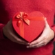 A woman's hands holding a red, heart-shaped box in front of her stomach