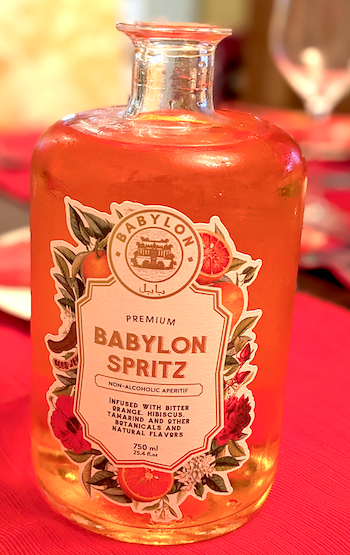 closeup of a bottle of Babylon Spritz on a red tablecloth with a wine glass in the background