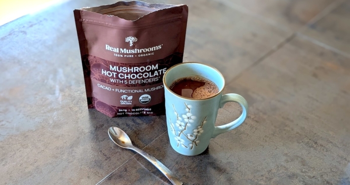 blue much of mushroom hot chocolate in front of the product package on a dark background