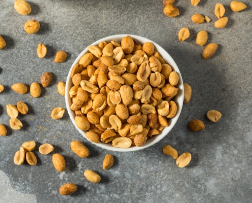 overhead shot of a bowl of roasted peanuts spilling out onto a gray countertop