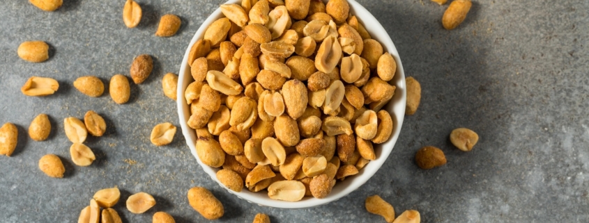 overhead shot of a bowl of roasted peanuts spilling out onto a gray countertop