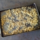 Crispy quinoa on a baking sheet with a white dish towel on the left and a bottle of olive oil and spoon on the right