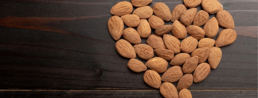 A closeup of roasted almonds in the shape of a heart on a black background
