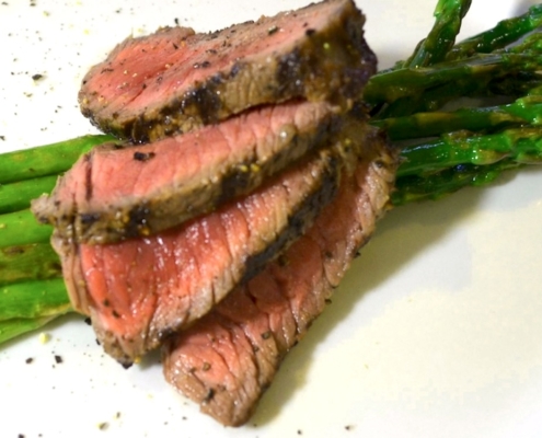 Grilled Bison Steak Recipe with an Easy Herb Marinade 2 closeup of four slices of the marinated, grilled bison steak on top of asparagus on a white plate