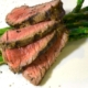 closeup of four slices of the marinated, grilled bison steak on top of asparagus on a white plate