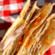 Closeup of the spicy peanut sandwich wrap being held over a red checkered tablecloth