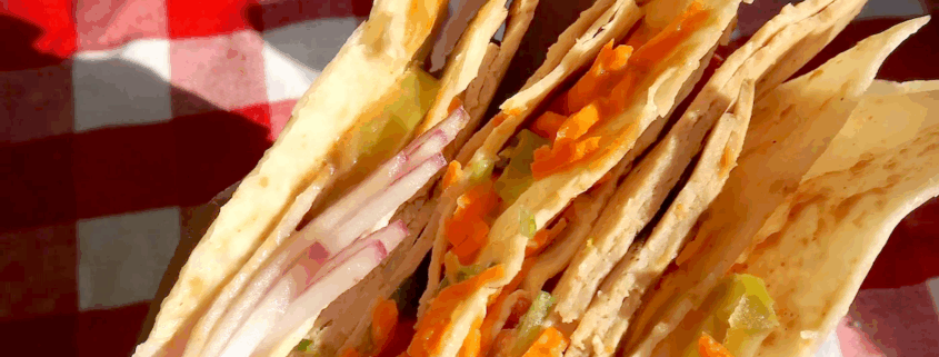 Spicy Peanut Vegan Sandwich Wrap 1 Closeup of the spicy peanut sandwich wrap being held over a red checkered tablecloth