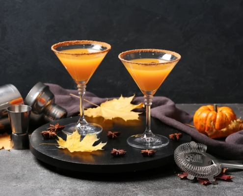 This Apple Pie Martini Tastes Like the Best Part of Apple Pie 1 two apple pie martinis on a black background surrounded by tiny pumpkins and cocktail making supplies