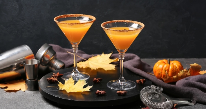 This Apple Pie Martini Tastes Like the Best Part of Apple Pie 1 two apple pie martinis on a black background surrounded by tiny pumpkins and cocktail making supplies