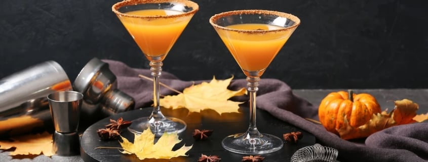 This Apple Pie Martini Tastes Like the Best Part of Apple Pie 1 two apple pie martinis on a black background surrounded by tiny pumpkins and cocktail making supplies