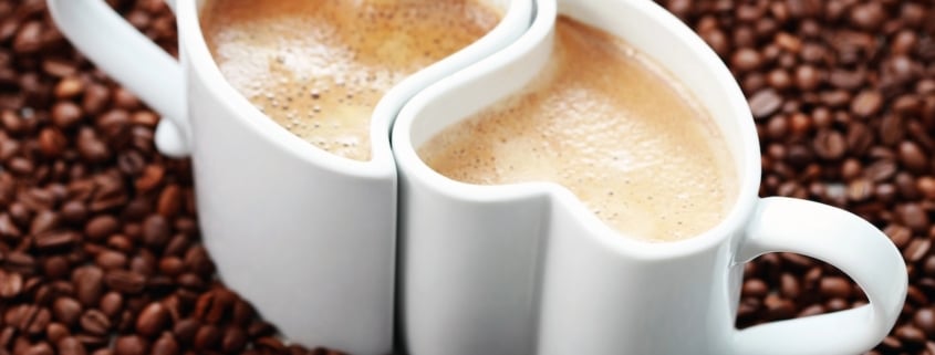 two interlinking white cups of coffee on a bed of coffee beans